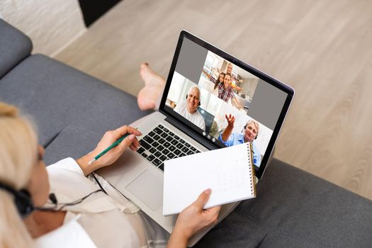 Back view of business woman talking to her colleagues about plan in video conference. Multiethnic business team using laptop for a online meeting in video call. Group of people smart working from home