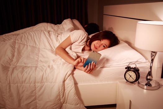 young woman using her mobile phone in bed at night while her husband is sleeping next to her