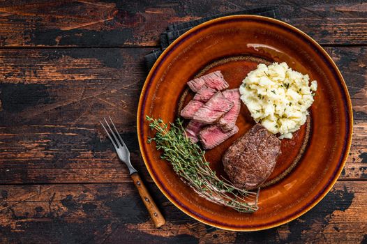 Sliced fillet mignon or tenderloin beef steak on a rustic plate with mashed potato. Dark wooden background. Top view. Copy space.