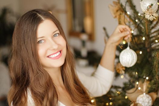 Decorating Christmas tree and winter holidays concept. Happy smiling woman holding festive ornament at home.
