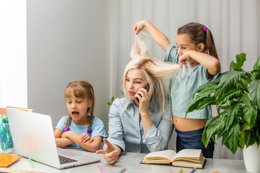 tired mother working at laptop and two little daughters playing