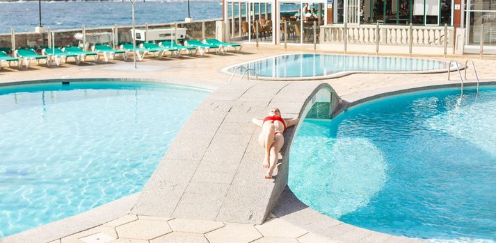 Young woman sunbathing near swimming pool.