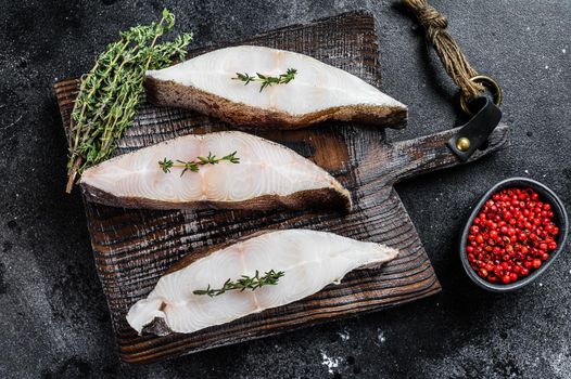 Raw fresh halibut fish steak on a wooden cutiing board. Black background. Top view.