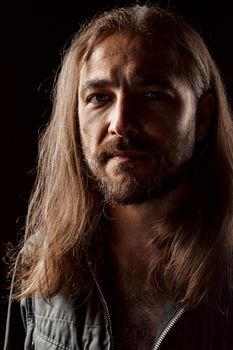 Long-haired masculine middle-aged man standing in the dark close up