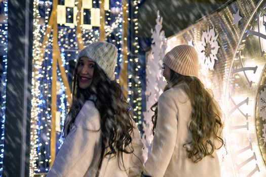 Two girlfriends asian girls in white coats are having fun hugging, new year, light bulbs