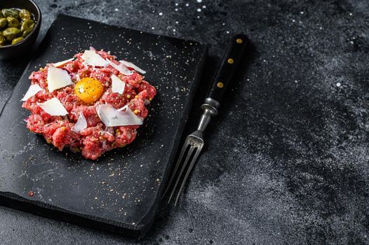 Tartar beef with a quail egg, capers and Parmesan cheese. Black background. Top view. Copy space.
