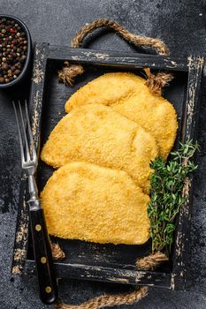 Raw chicken cordon bleu meat cutlets in a wooden tray with herbs. Black background. Top view.