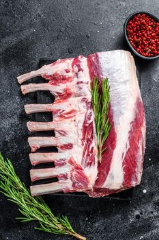 Raw fresh rack of lamb meat on marble board. Black background. Top view.