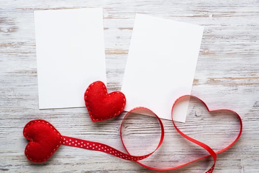 Flat lay composition with red love hearts and ribbon. Blank sheet of white paper on vintage wooden table. Declaration of love letter. Saint Valentine's day congratulation. Romantic event invitation.