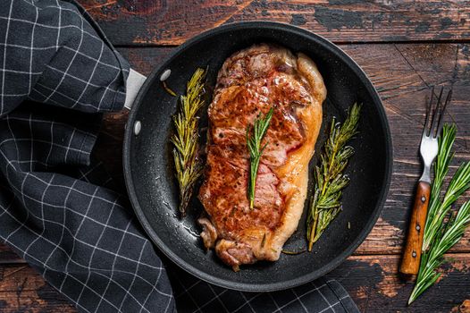 Grilled new york strip beef meat steak in a pan with herbs. Dark wooden background. Top view.