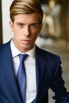 Portrait of an attractive young businessman in urban background wearing blue suit a necktie. Blonde hair