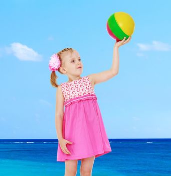 little girl in a pink dress holding at arm's length ball on the background of blue sea