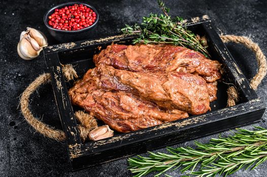 Raw marinated brisket steaks in a wooden tray with herbs. Black background. Top view.