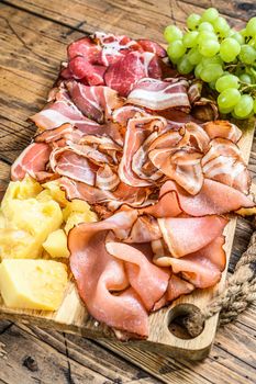 Meat antipasto board, pancetta, salami, sliced ham, sausage, prosciutto, bacon with grape and parmesan cheese. Wooden background. Top view.