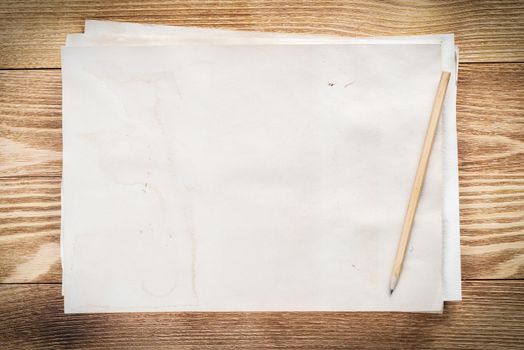 Artist workplace with sheet of paper and pencil lying on wooden desk. Rectangular white paper stack with blank copy space. Textured natural wooden background. Art school template for advertising