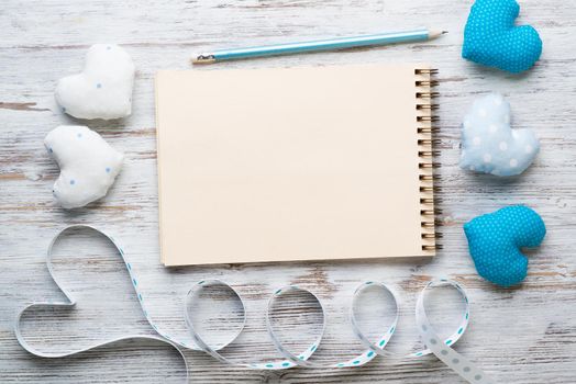 Flat lay elegant composition with blue and white handmade fabric hearts. Open sketchbook with pen on vintage wooden table. Saint Valentine's day congratulation. Romantic dating invitation.