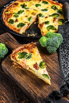 Quiche tart with smoked salmon, broccoli and spinach. Dark wooden background. Top view.