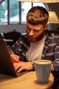 Casual business man or freelancer planning his work on notebook, working on laptop computer with smart phone, cup of coffee on table at coffee shop or home office, working from cafe concept