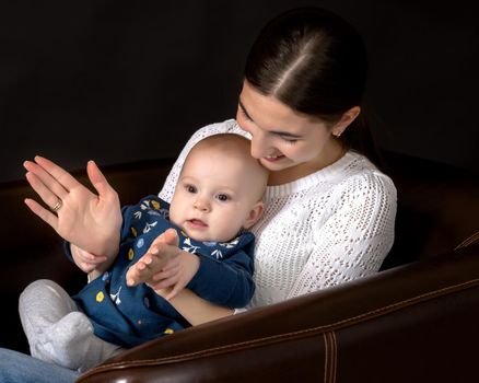 Beautiful young mother with a little daughter in her arms, studio on a black background. The concept of a happy childhood, advertising.