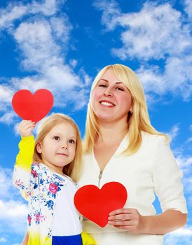 Cute little girl and her mother holding the heart.On the background of summer blue sky and fluffy clouds.