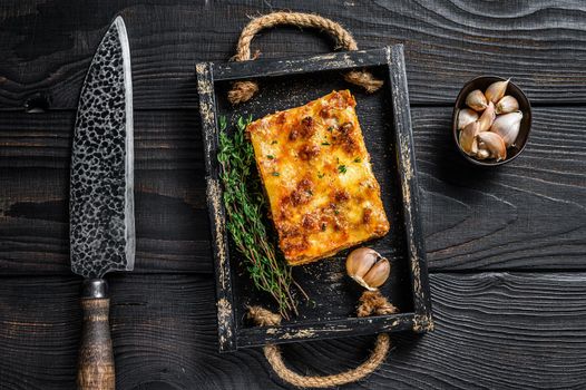 Portion of Lasagna with mince beef meat and tomato bolognese sauce in a wooden tray. Black wooden background. Top view.