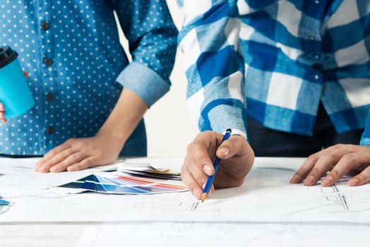 Professional designers discussing architecture project. Creative teamwork and project brainstorming. Close up human hands and construction drawing of building on desk. Industrial engineering company.