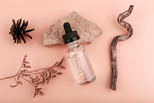 Top view of skin serum in transparent bottle with black cap on beige table with dry flower, stone, cone and stick near. Concept of natural organic cosmetics and spa or anti aging treatment