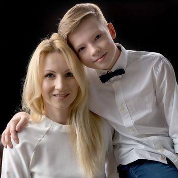 Mom and son teenager on a black background. The concept of happy childhood, People, harmonious development of the child in the family.