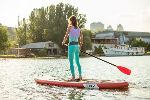 Woman is floating on a SUP board on sunny morning. Stand up paddle boarding - awesome active recreation during vacation. Back view.