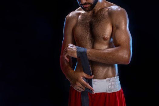 Boxer preparing her gloves for a fight. Photo of muscular man strapping up hands on black background. Strength and motivation. Studio shot