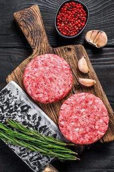 Raw steak cutlets with mince beef meat and rosemary on a wooden cutting board with meat cleaver. Black Wooden background. Top view.