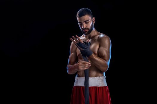 Boxer preparing her gloves for a fight. Photo of muscular man strapping up hands on black background. Strength and motivation. Studio shot