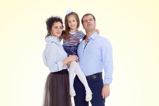 Happy young family, mom dad and little daughter.Parents keep the girl in her arms , and she hugs their neck.On a yellow gradient background.