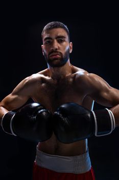 Young male boxer wearing his red boxing shorts and gloves on black background. Sports concept