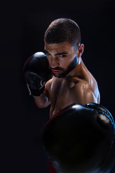 Man is hitting an opponent. Focused fighter with naked torso and boxing gloves looking at the camera. Win. Studio shot on a black background