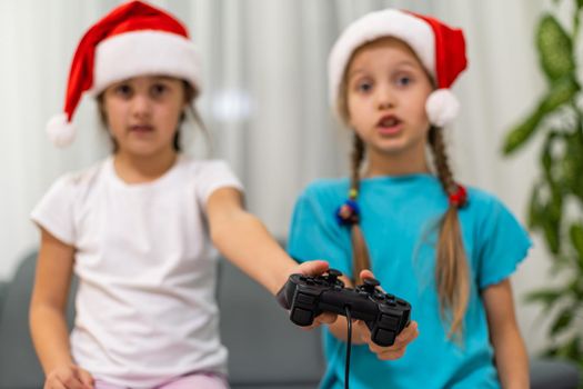 Portrait of two nice sweet pretty lovely attractive charming funny cheerful positive girls in santa hats sitting on divan playing video device battle