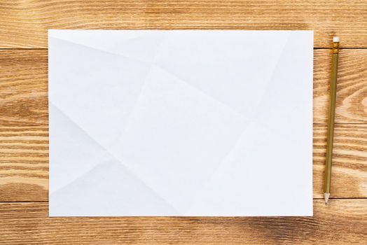 Business workspace with sheet of paper and pencil lying on wood table. View from above with copy space. Rectangular blank white paper on textured natural wooden background. Business presentation