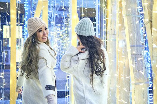 Two girlfriends asian girls in white coats are having fun hugging, new year, light bulbs