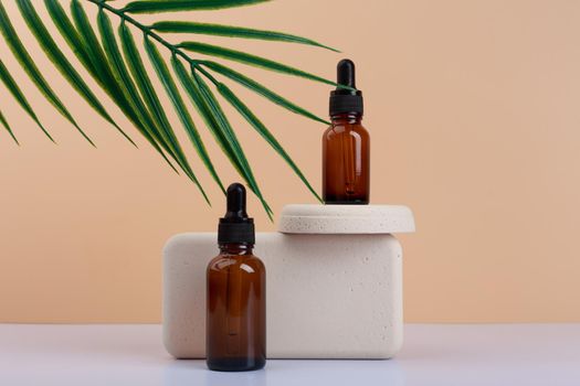Two dark bottles with skin serum or oil for nails with beige geometric props on white table against beige background decorated with palm leaf. Concept of luxury organic skin care or manicure products