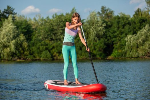 Woman is floating on a SUP board on sunny morning. Stand up paddle boarding - awesome active recreation during vacation. Yoga on sup board with paddle