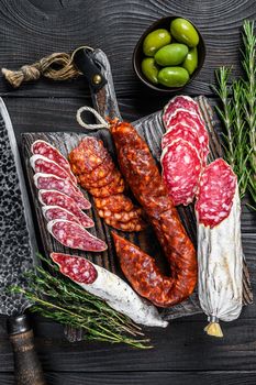 Spanish tapas sliced sausages salami, fuet and chorizo on a wooden cutting board. Black wooden background. Top view.