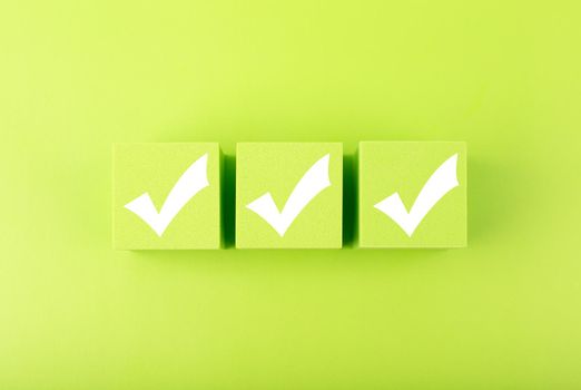 Three white checkmarks on green toy cubes on bright background. Concept of questionary, checklist, to do list, planning, business or verification.