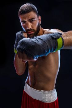 The boxer is ready to deal a powerful blow. Photo of muscular man with strong hands and clenched fists in blue stripes on black background. Strength and motivation. Studio shot