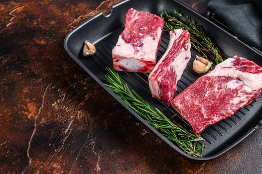 Beef calf short ribs meat in a grill pan ready for cooking. Dark background. Top view. Copy space.