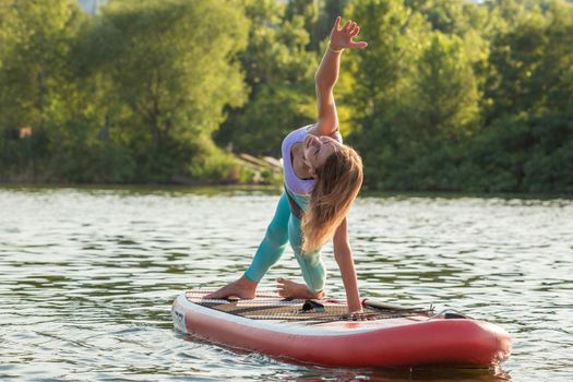 Young woman doing yoga on sup board with paddle. Yoga pose, side view - concept of harmony with the nature, free and healthy living, freelance, remote business.