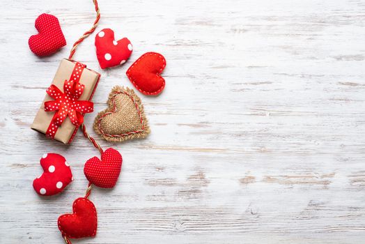 Flat lay cute composition with handmade fabric red hearts. Gift box with ribbon bow on wooden table. Happy birthday or anniversary congratulation. Merry Christmas and Happy New Year card.