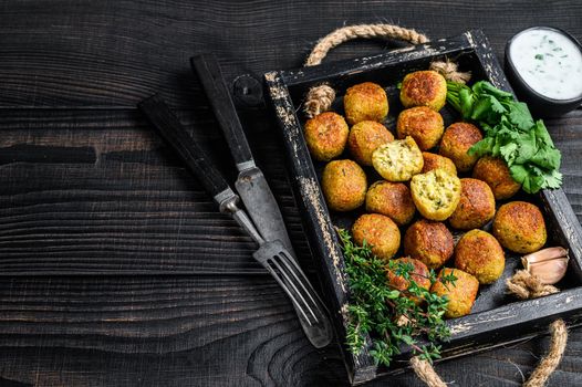 Roasted chickpeas falafel balls with garlic yogurt sauce in a wooden tray. Black wooden background. Top view. Copy space.