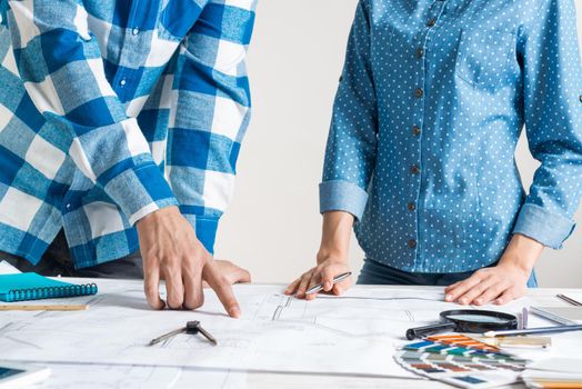 Man and woman together working at design project. Creative teamwork at workspace with construction blueprint and color swatches. People standing near desk and discussing in architecture studio.