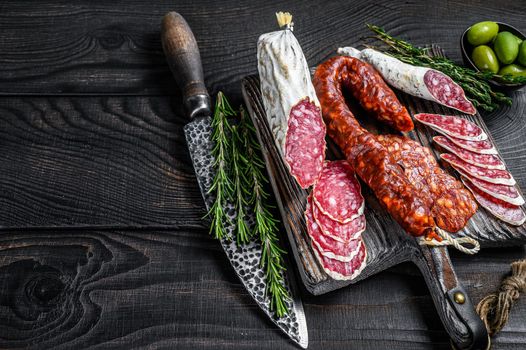 Spanish tapas sliced sausages salami, fuet and chorizo on a wooden cutting board. Black wooden background. Top view. Copy space.