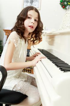 Adorable little girl new year's eve on the backdrop of the Christmas tree plays the piano.